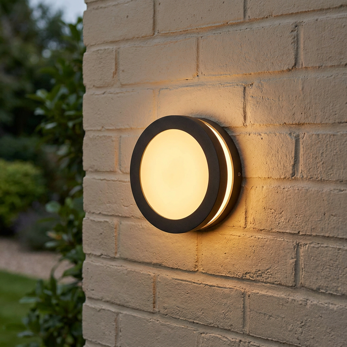 Circular black outdoor lantern with a warm light glow mounted on a white brick wall.