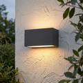 Elstead Asker Graphite Outdoor Wall Light on a white textured wall, casting warm light upwards and downwards.