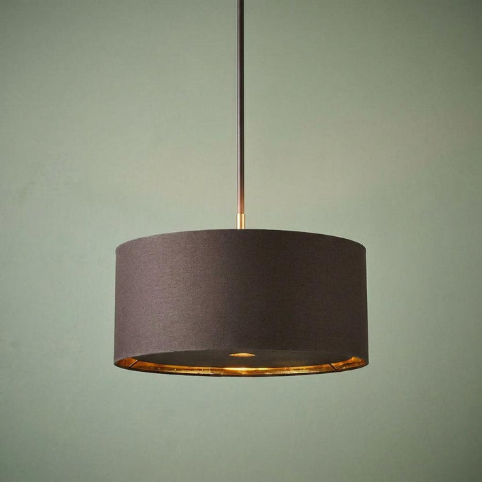 Brown drum pendant light with polished brass interior and stem against a pale green wall.