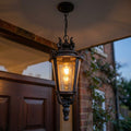 Weathered bronze outdoor pendant lantern with seeded glass panels hanging illuminated outside a house at dusk.