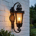 Elstead Baltimore weathered bronze outdoor wall lantern with ornate scrollwork glowing on a white brick wall.