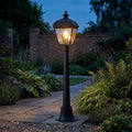Elstead Bayview black medium outdoor bollard light illuminating a stone garden path at dusk.