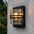 Modern black outdoor wall light with curved clear glass and horizontal bands mounted on a white textured wall.
