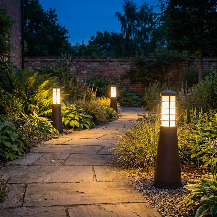 Three Elstead Beta Aged Iron garden bollard lights illuminating a stone garden path at dusk.