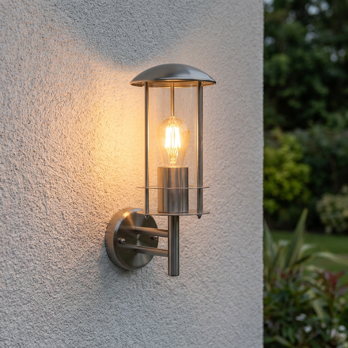 Stainless steel outdoor wall lantern with a warm LED bulb mounted on a white textured exterior wall.