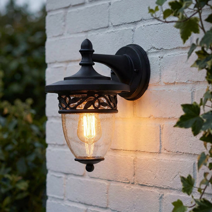 Elstead Burford outdoor wall light in black with seeded glass and a glowing bulb mounted on a white brick wall.