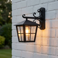 Black Elstead Canterbury outdoor wall lantern with warm illumination mounted on a white brick wall.