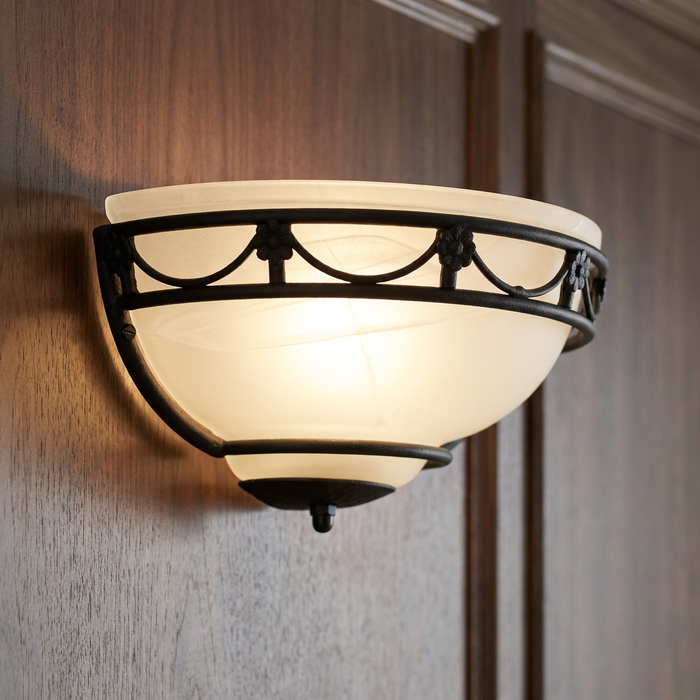 Elstead Carisbrooke Wall Uplighter with black floral wrought iron frame and frosted glass shade on a wood wall.