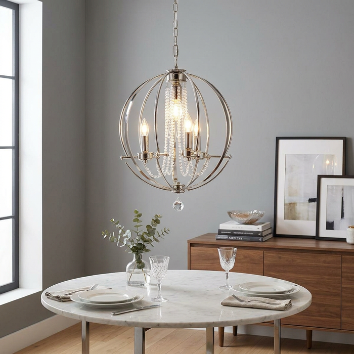 Polished nickel orbital chandelier with crystal accents hanging over a marble dining table in a grey room.