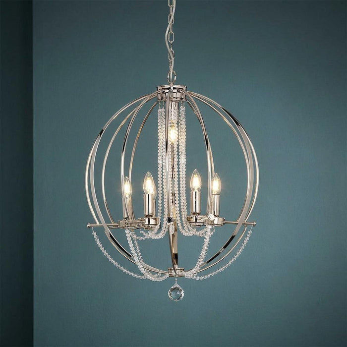 Polished nickel orb chandelier with crystal bead drapes and candle-style bulbs against a teal wall.