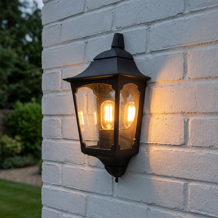 Traditional black outdoor half-lantern with a warm glowing bulb mounted on a white painted brick wall.