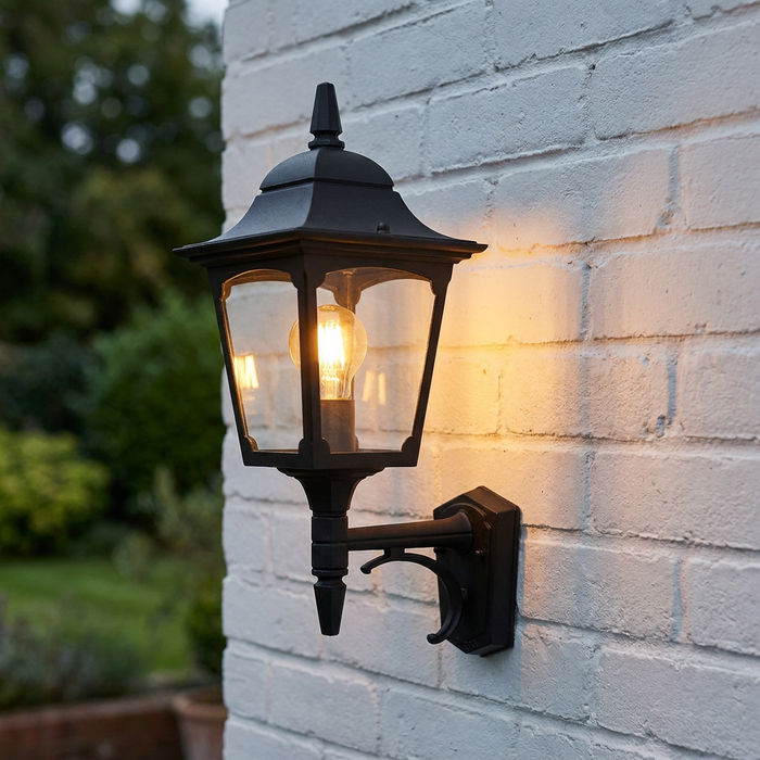 Elstead Chapel black outdoor uplighter wall lantern with a lit bulb mounted on a white brick wall.