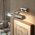 Polished nickel picture light with adjustable arms mounted on a wall, illuminating a framed artwork below.
