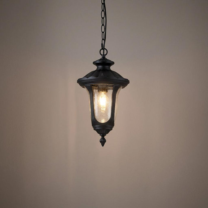 Black hanging outdoor lantern with seeded glass and a glowing bulb against a neutral background.