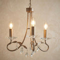 Three-light chandelier in silver and gold with leaf details and crystal droplets, hanging against patterned wallpaper.