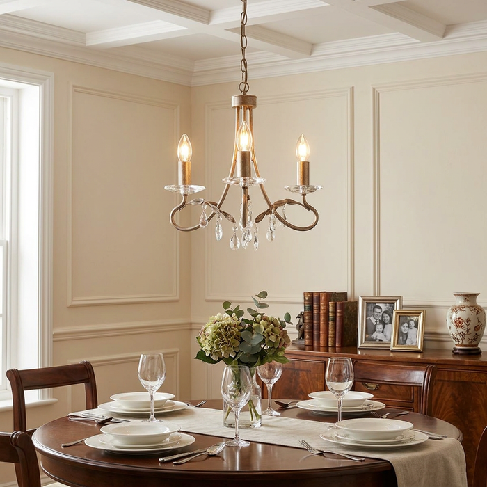 Three-light silver and gold chandelier with crystal accents hanging above a set dining table in a classic room.