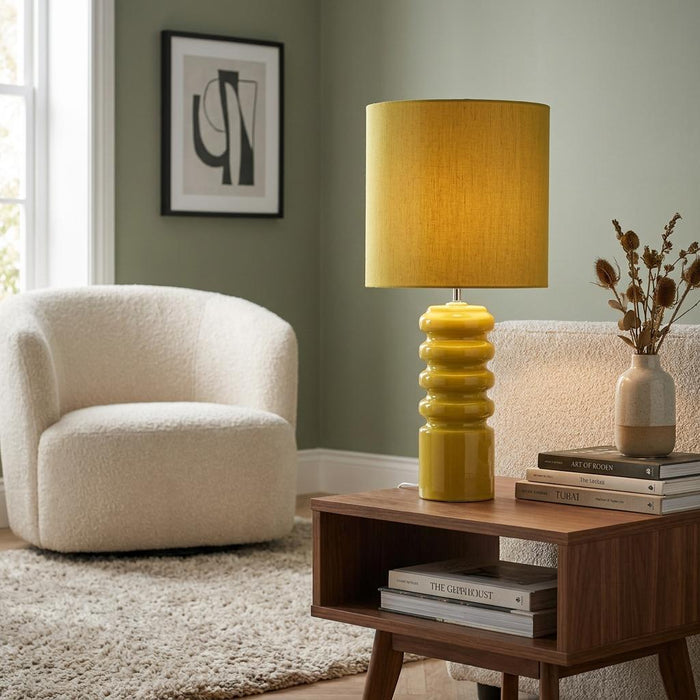 Lime glaze ceramic table lamp with a contoured base and lime shade on a wooden table in a green-walled living room.