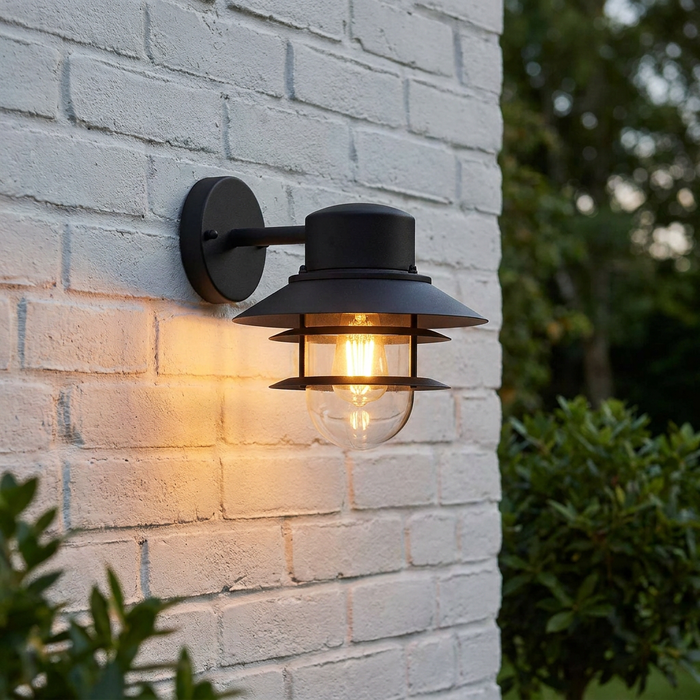 Black Elstead Copenhagen outdoor wall light with tiered shades and a warm glowing bulb on a white brick wall.