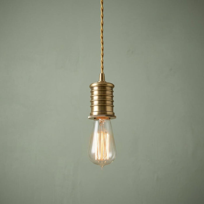 Aged brass industrial pendant light with an Edison filament bulb against a muted green wall.