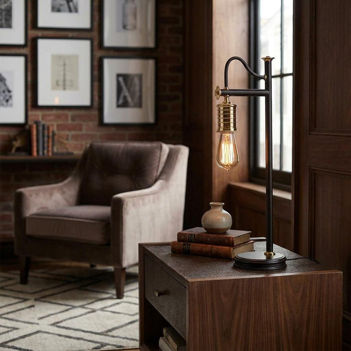 Industrial black and brass table lamp with an exposed bulb on a wooden side table in a moody living room.