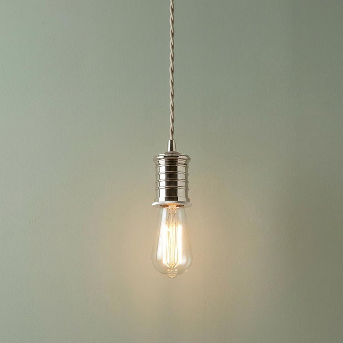 Polished nickel pendant light with a lit Edison bulb and twisted cord against a sage green wall.