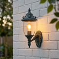 Traditional verdigris outdoor wall light with clear glass and warm glowing bulb on a white brick wall.