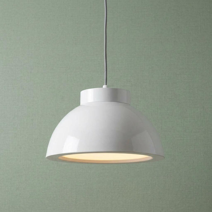 Glossy white dome LED pendant light emitting warm light against a textured green background.