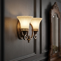 Elstead Feiss twin arm walnut wall light with cream glass shades on a dark paneled wall.