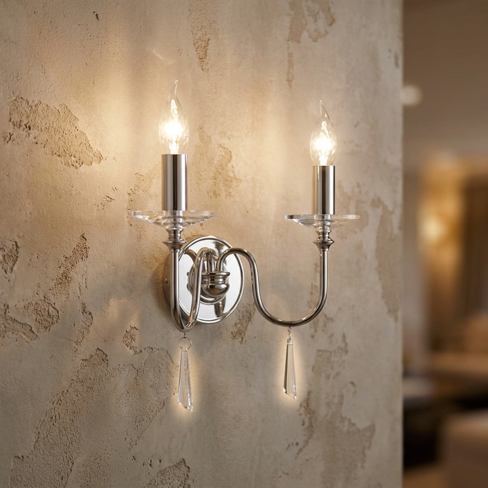Polished chrome two-light wall sconce with crystal drops mounted on a textured beige wall.