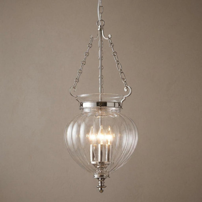 Three-light polished nickel ceiling lantern with clear ribbed glass globe hanging against a neutral wall.