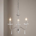 Polished nickel 3-light chandelier featuring glass accents and lit candle bulbs against a neutral wall.