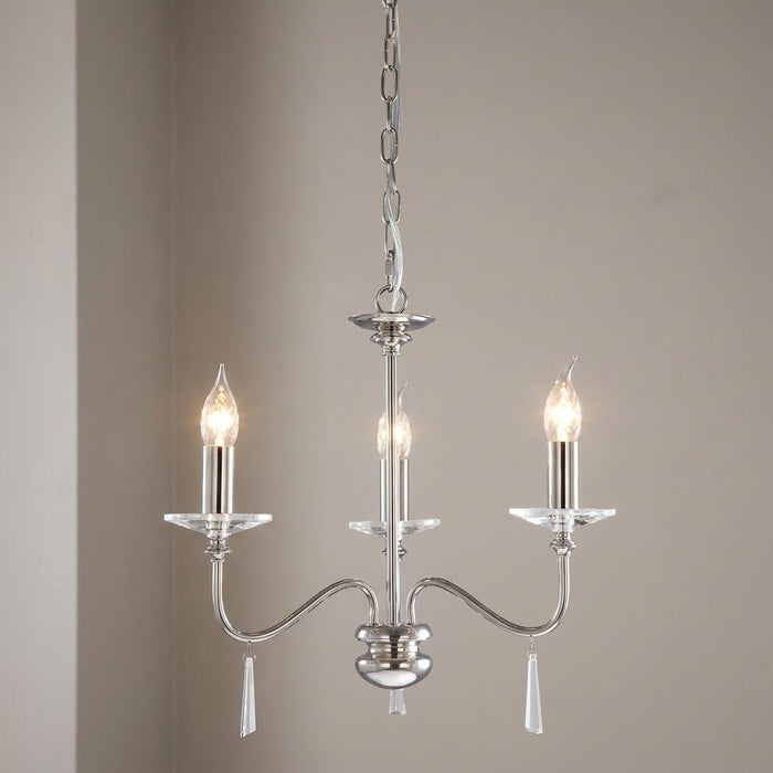 Polished nickel 3-light chandelier featuring glass accents and lit candle bulbs against a neutral wall.