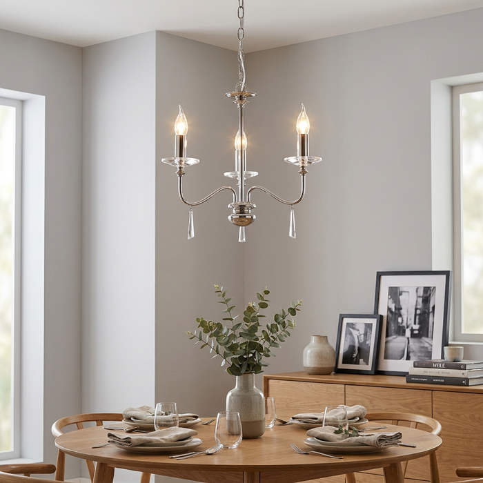 Three-light polished nickel chandelier with crystal droplets hanging above a wooden dining table in a neutral room.