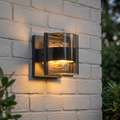 Modern grey outdoor wall light with curved glass and warm glow mounted on a white brick wall.