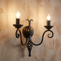 Elstead Harlech black 2-light wall light with scroll arms and flame bulbs on a textured wall.