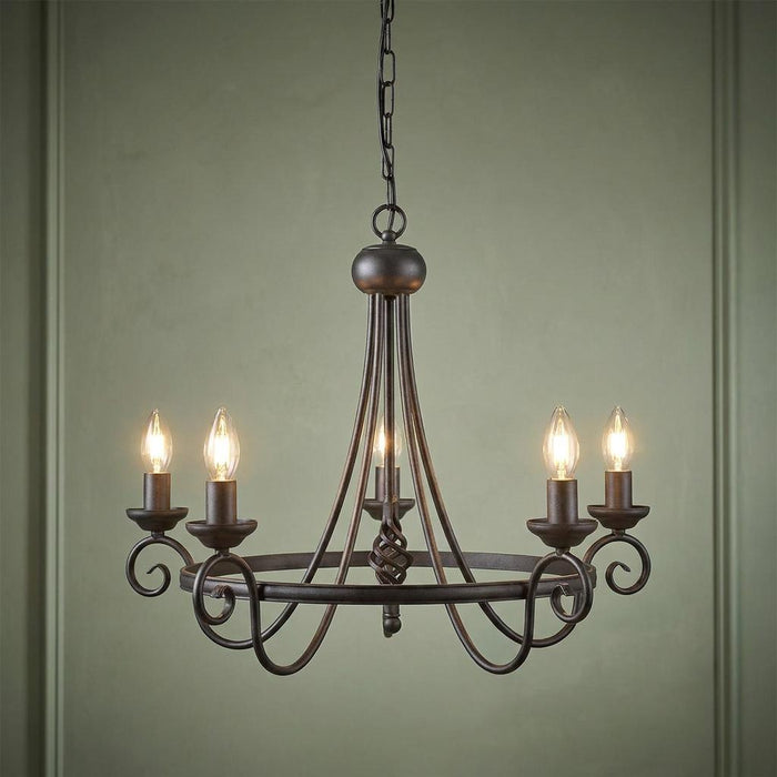 Elstead Harlech 5-light black chandelier with scrolled metal arms and glowing candle bulbs against a green wall.