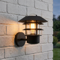 Black Elstead Helsingor outdoor wall light with a lit Edison bulb mounted on a white brick wall.
