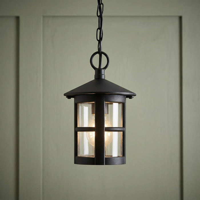 Black lantern-style outdoor pendant light with clear glass panels hanging against a pale green paneled wall.