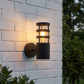 Elstead Hornbaek black outdoor wall light with a glowing bulb mounted on a white painted brick wall.
