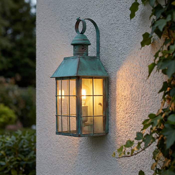 Traditional verdigris outdoor wall lantern with a warm glowing bulb mounted on a textured exterior wall next to ivy.