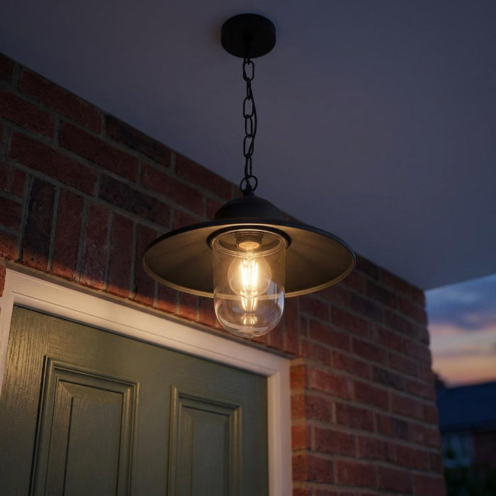 Elstead Karlstad black outdoor pendant light with a clear glass shade, hanging above a green door at dusk.