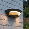 Semi-circular graphite wall light emitting a warm glow on a white painted brick wall.