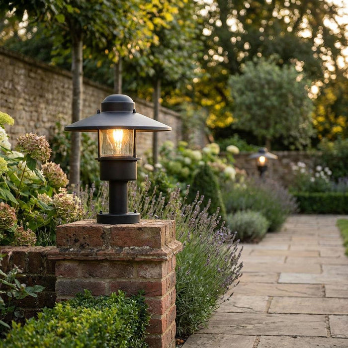 Modern black garden light on a brick pier, illuminating a stone path through a lush flower garden.