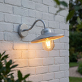 Elstead Klampenborg silver outdoor wall light with a warm bulb, mounted on a white brick wall.