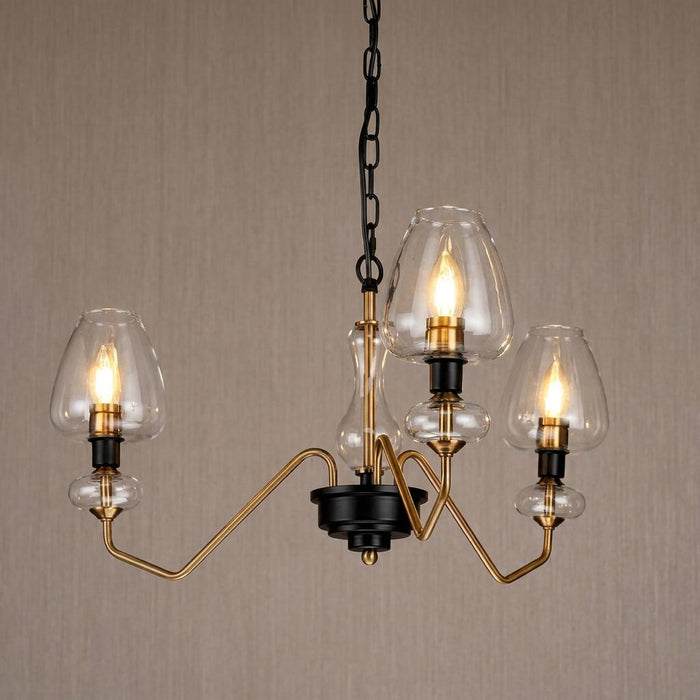 Armand 3-light brass and black ceiling pendant with clear glass shades and warm lit bulbs against a beige wall.