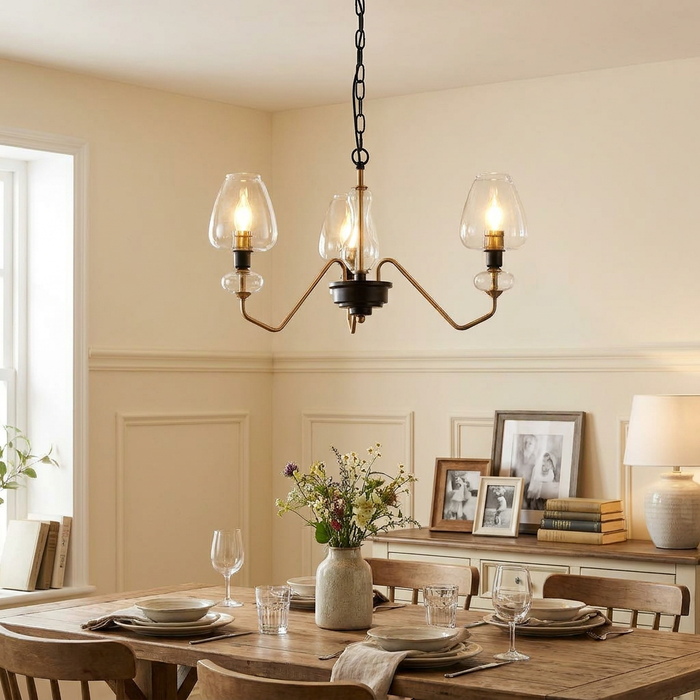 A three-light brass ceiling pendant with clear glass shades hanging over a rustic wooden dining table.
