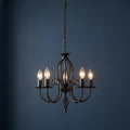 Five-light black wrought iron chandelier with lit candle bulbs and scrollwork against a dark blue wall.