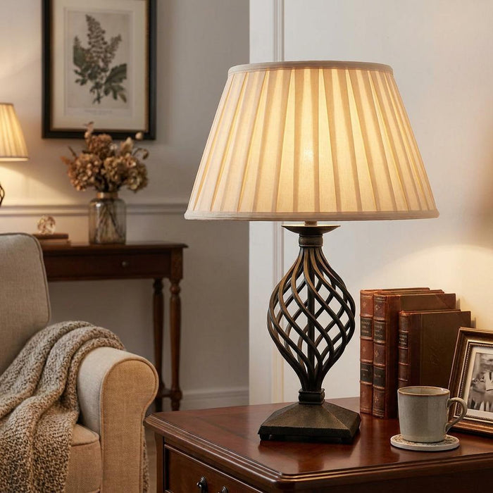 Belfry table lamp with an open cage iron base and pleated cream shade on a wooden table in a warm living room.