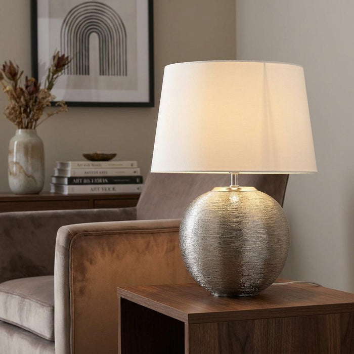 Elstead Lighting Caesar silver textured spherical table lamp with a white drum shade on a wooden side table.