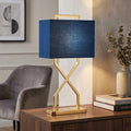 Polished gold table lamp with a geometric X-shaped base and a rectangular navy blue fabric shade.